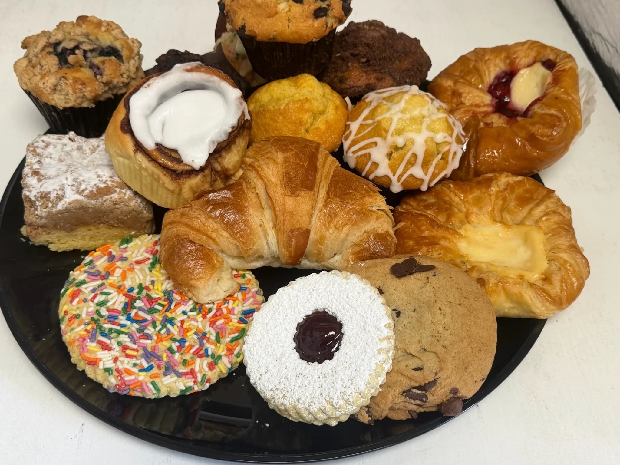 A bakery platter overflowing with fresh muffins, croissants, danishes, and cookies