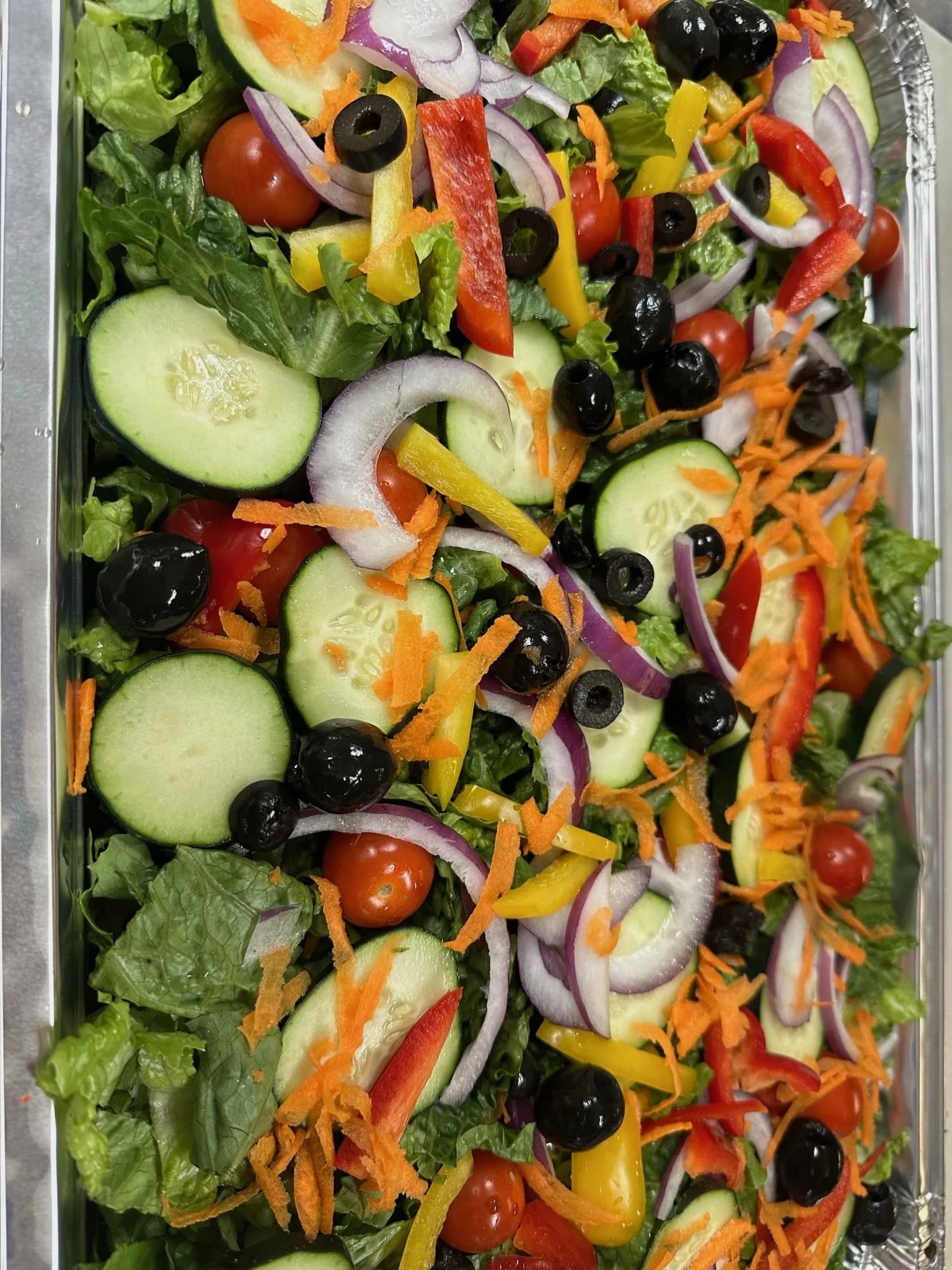 A large chopped salad — cucumbers, peppers, olives, tomatoes, and red onions over crisp greens