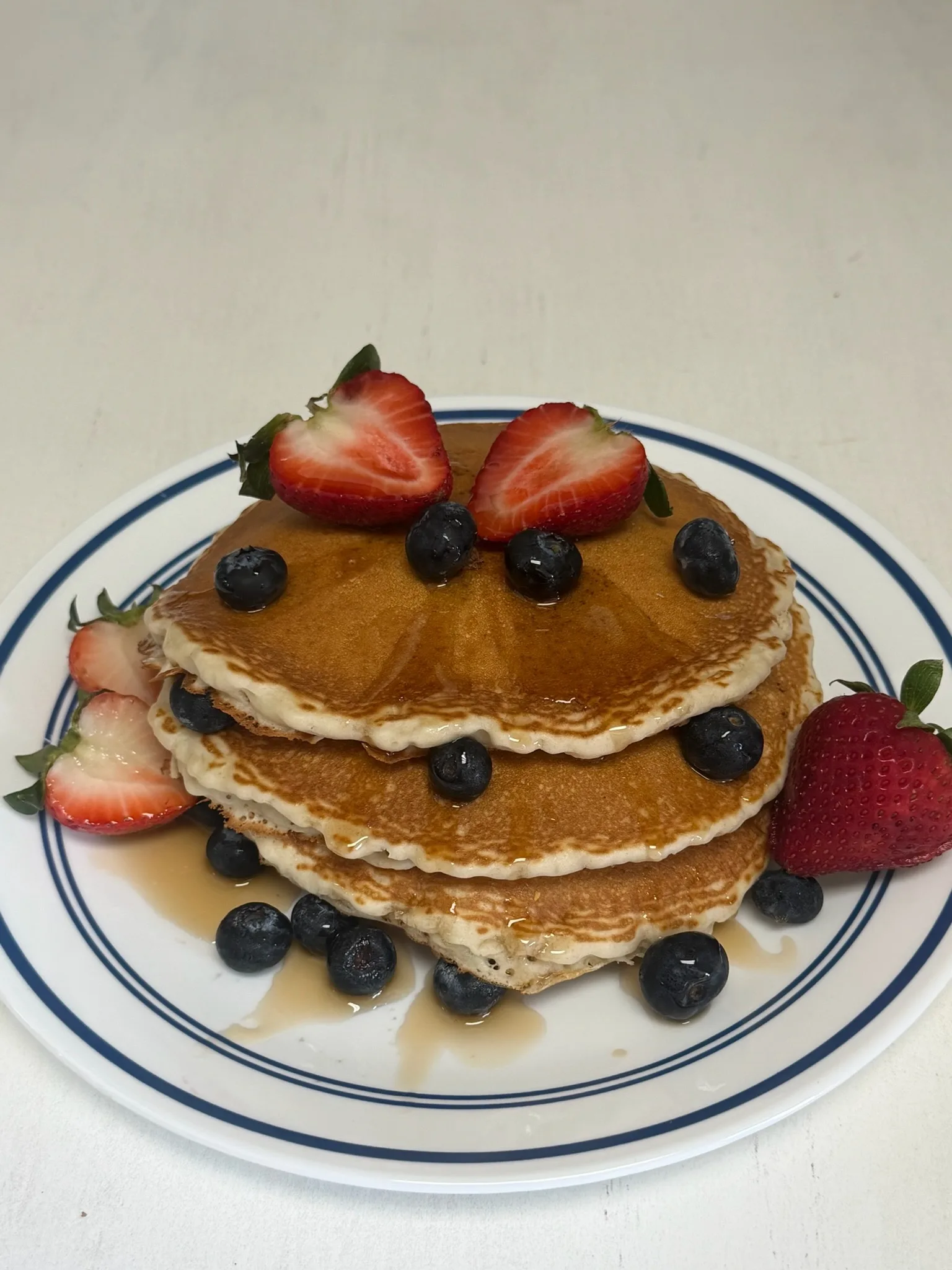 A fluffy pancake stack topped with strawberries, blueberries, butter, and maple syrup