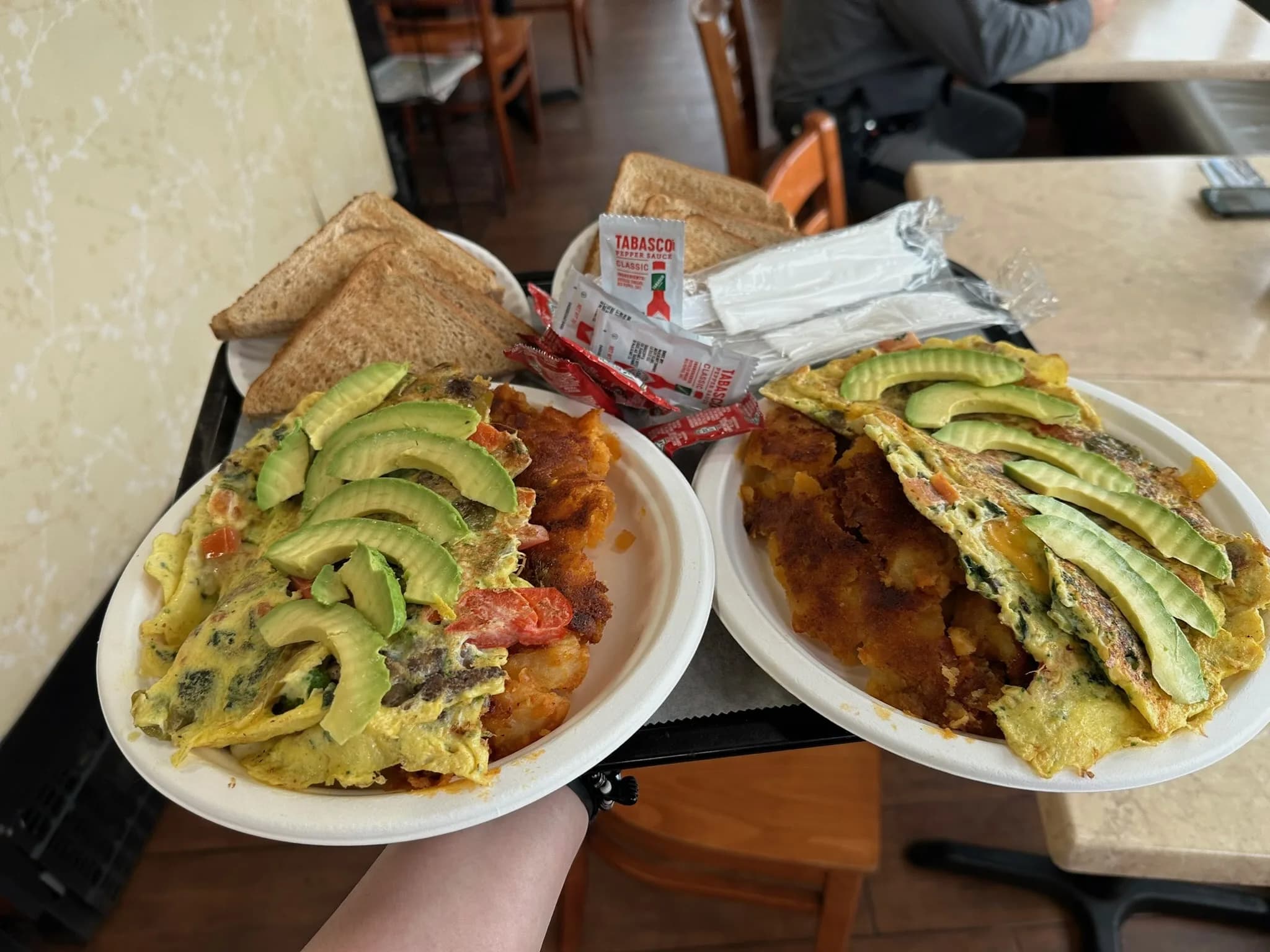An omelette spread — three plates with home fries, toast, and a side of avocado