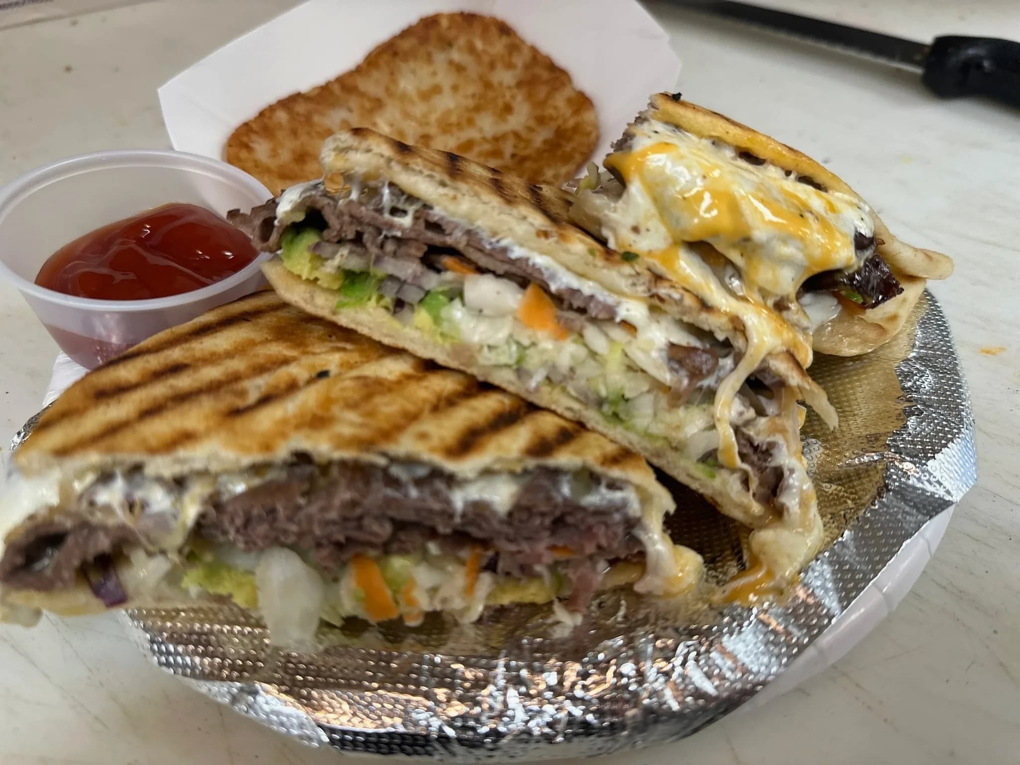 The Philly Cheesesteak — grilled roast beef with caramelized onions, peppers, and cheese sauce, pressed crisp