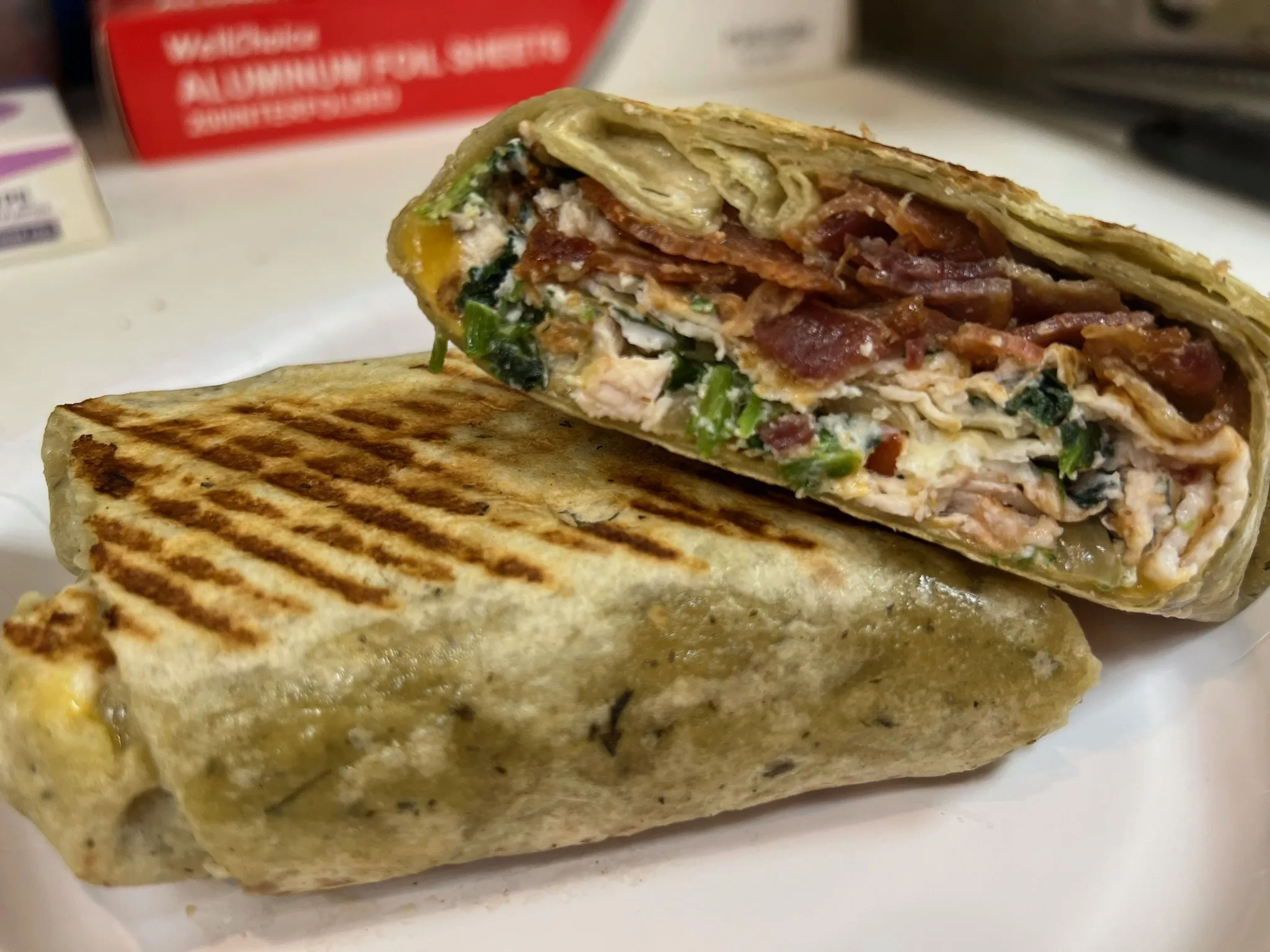 Pressed breakfast wrap, sliced open — bacon, chicken, melted cheese, and fresh greens in a spinach tortilla