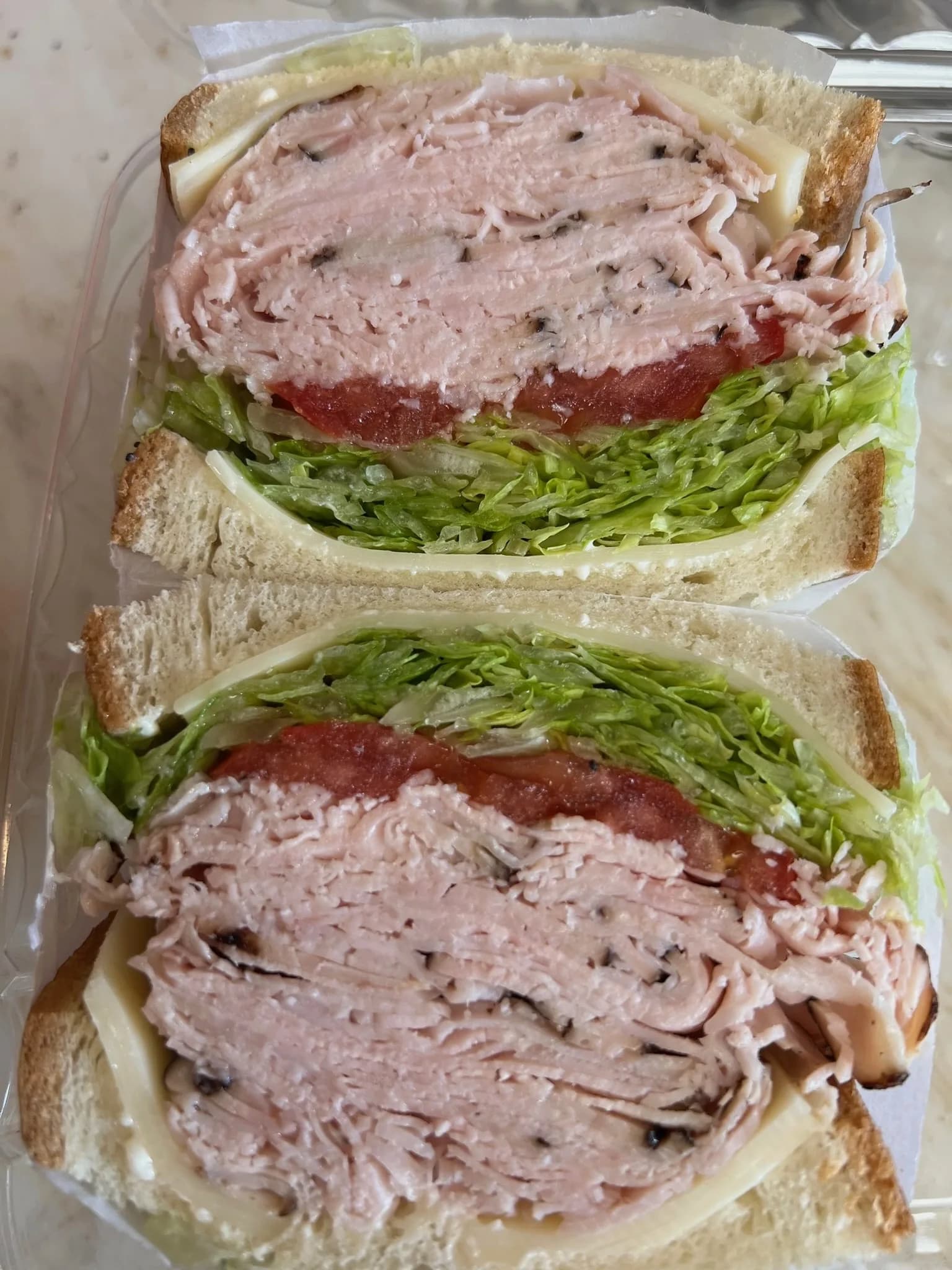 Stacked turkey breast sandwich with lettuce, tomato, and cheese on fresh-baked bread